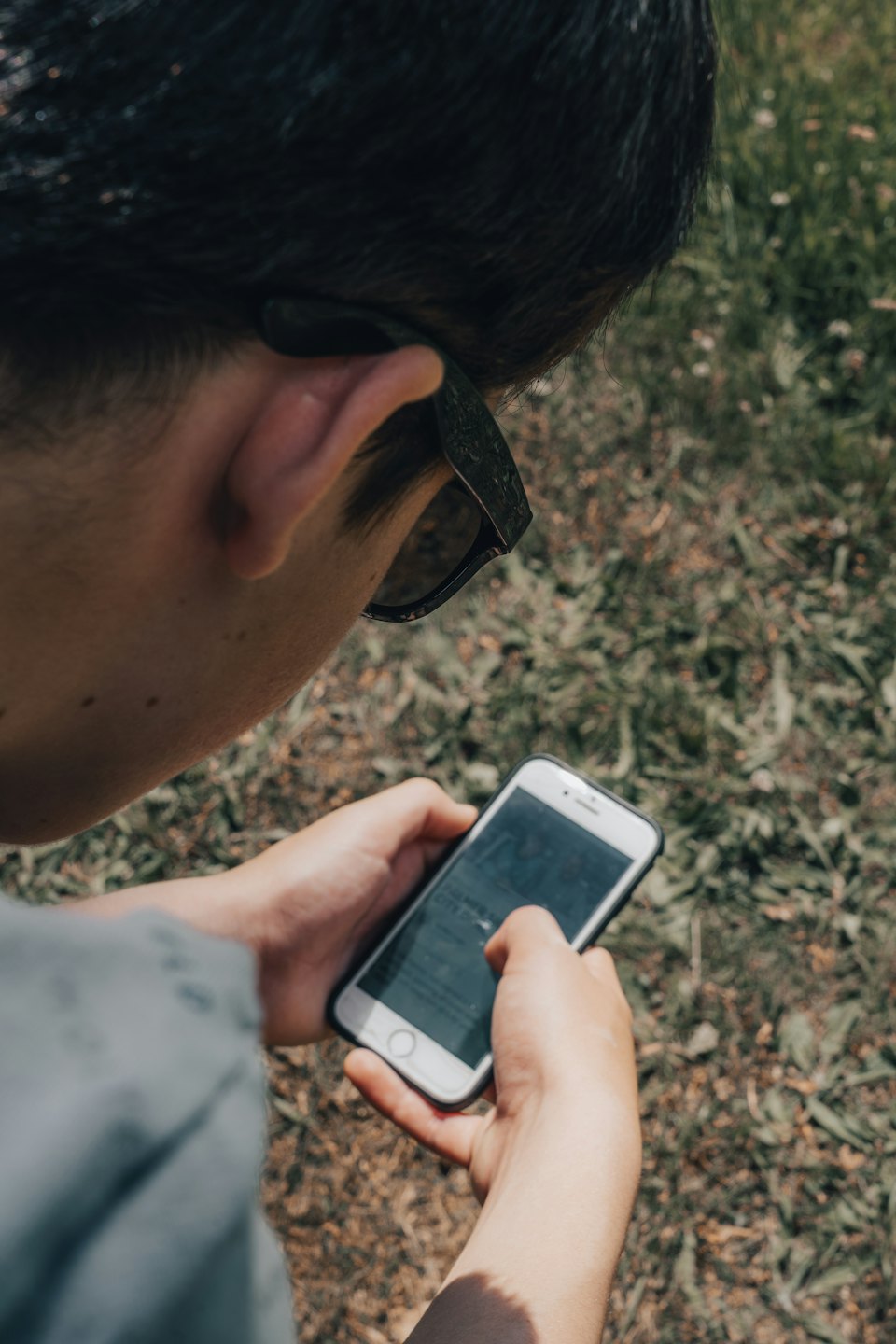 Hands tapping on a white smartphone screen outdoors.